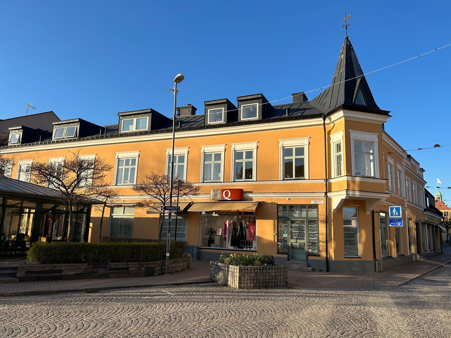 Ockragul hörnfastighet med torn och lokaler i gatuplan vid ett kullerstenstorg i Sölvesborg.